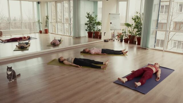 Group of young women lying in corpse pose during yoga class in studio.