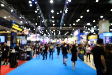 Fototapeta premium A vibrant, blurry view of a crowded indoor exhibition or trade show with bright lights and people walking on a blue carpet.