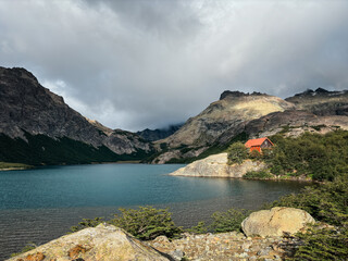 Rugged mountain peaks with a red-roofed cabin by a blue lake