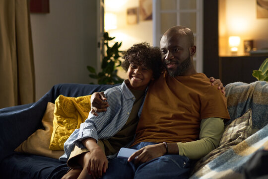 African American father and his young son smiling while sitting on cozy couch together, enjoying quality bonding time at home without electronic devices present