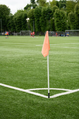 A bright orange corner flag stands on a well-maintained green soccer field, where players are actively participating in a practice session on a sunny afternoon © Oleksandr Zinchenko