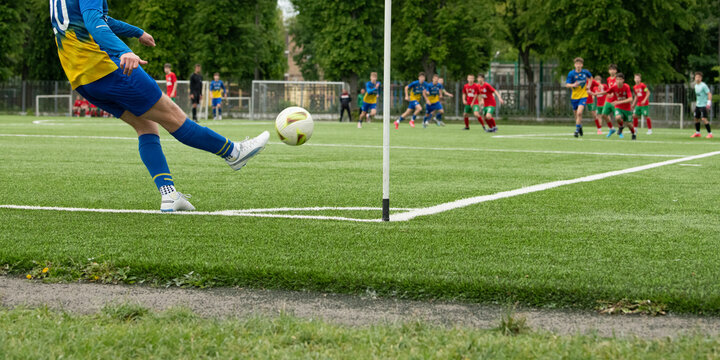 A soccer player prepares to take a corner kick while teammates and opponents engage in an exciting match. The vibrant green turf contrasts with the colorful uniforms worn by the players
