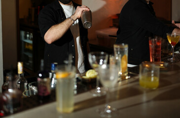 Close-up of a bartender hands shaking a metal cocktail shaker at bar counter.