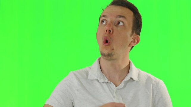 A man in a white shirt gestures dramatically by fanning himself and puffing out his cheeks to represent feeling hot or exhausted while standing before a green screen. Concept of hard work, global warm