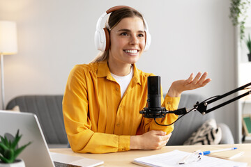 Smiling woman recording podcast wearing headphones and talking into microphone