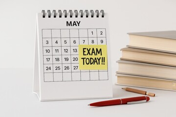 Calendar on May with a sticky note marked Exam Today next to a stack of books and a red pen. Educational concept about exam day, study time, and academic schedule reminder