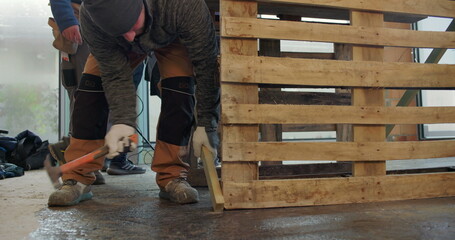 Worker adjusting wooden pallet on construction site floor, hands-on labor, close-up of manual work,...