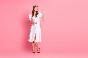 Young elegant woman in white dress with hand gesture standing on pink background, promoting style...