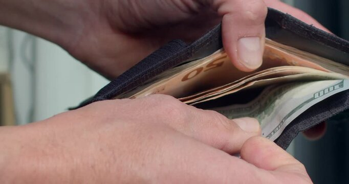 This image features a closeup view of an individual holding a wallet that is packed with various denominations of cash