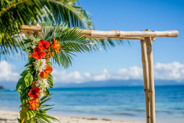 Tropical wedding arch adorned with bright, exotic flowers like hibiscus and orchids, with palm leaves and a sunny beach view