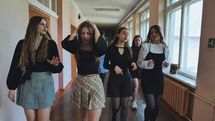 Teenage girls strolling through school hallway, chatting and gesturing happily after class