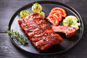 Barbecue grilled pork ribs with boiled potatoes and fresh vegetables, black background