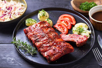 Barbecue grilled pork ribs with boiled potatoes and fresh vegetables, black background