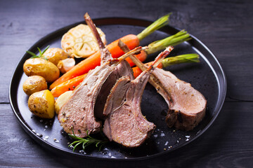 Lamb chops with carrots and potatoes, black background. Roasted rack of lamb