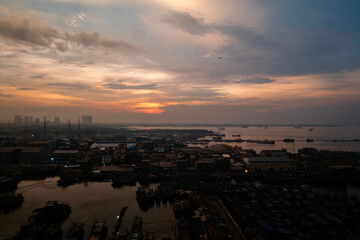 A vibrant sunset over Jakarta, with warm orange and red hues reflecting on the water, creating a dramatic and serene atmosphere.