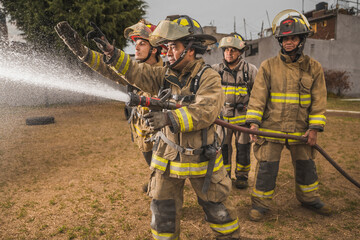 Four brave firefighters standing behind a curtain of water in an epic pose putting out a fire.