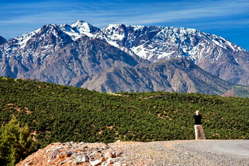 A female figure against backdrop of snow-capped mountain peaks. Morocco, High Atlas Range. Blue...