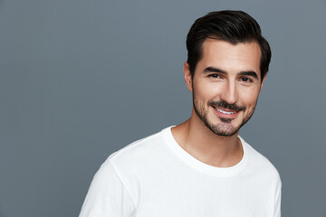 Obraz premium Smiling man in casual white t-shirt poses confidently against a grey background, showcasing a friendly expression and engaging demeanor. Portrait photography concept.