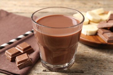 Tasty chocolate milk, pieces and banana on wooden table, closeup