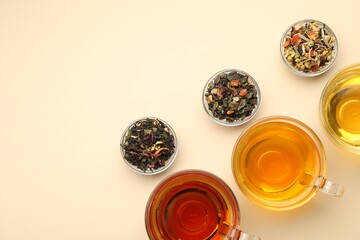 Different freshly brewed teas and dry leaves on beige background, flat lay. Space for text