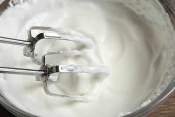 Hand mixer with whisks and bowl of whipped cream on table, closeup
