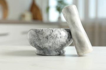 Mortar and pestle on white marble table in kitchen, closeup