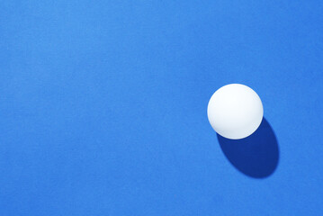 One ping pong ball on blue background, top view. Space for text