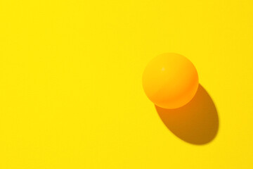 One ping pong ball on yellow background, top view. Space for text