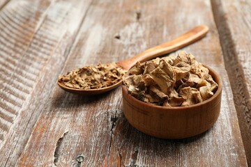 Pieces of dry chicory roots in bowl and spoon on wooden table, closeup