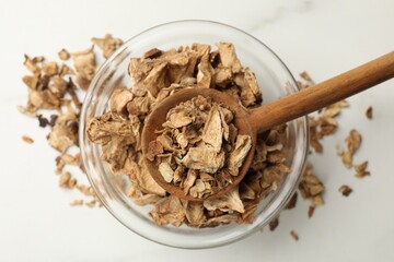 Pieces of dry chicory roots in bowl and spoon on white table, top view
