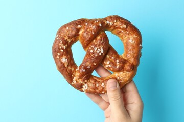 Woman with tasty pretzel on light blue background, closeup