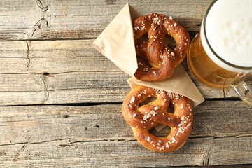 Tasty pretzels and glass of beer on wooden table, flat lay. Space for text