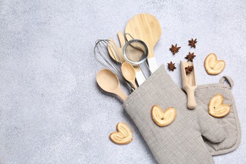 Different kitchen utensils in oven mitten, cookies and anise stars on light table, flat lay. Space for text