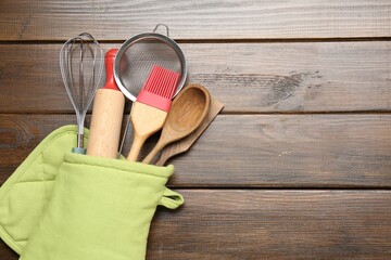 Different kitchen utensils in oven mitten on wooden table, top view. Space for text