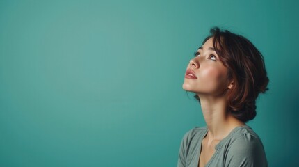 Fototapeta premium Beautiful young woman looks up with curiosity on teal background 