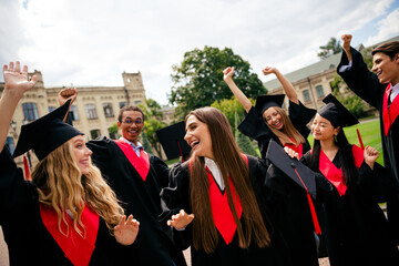Joyful graduates celebrate outside university, wearing caps and gowns, with excitement. Friends...