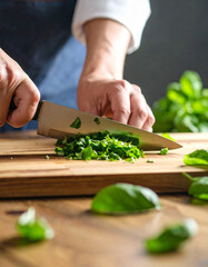 Green herbs like basil are being chopped finely on a wooden surface, releasing their fresh aromatic...