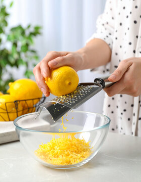 Bright yellow lemon zest is being grated with a zester over a clear glass bowl, adding citrus flavor.