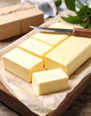 Creamy white butter is being cubed with a knife on a parchment-lined tray, ready for baking.