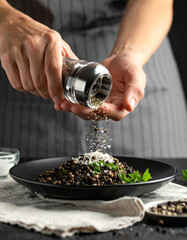 Crushed black peppercorns are being sprinkled over a dish from a glass grinder, adding spice.