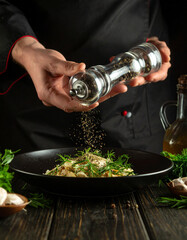 Crushed black peppercorns are being sprinkled over a dish from a glass grinder, adding spice.