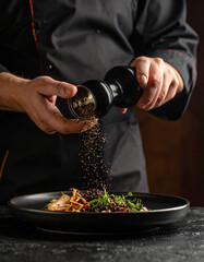 Crushed black peppercorns are being sprinkled over a dish from a glass grinder, adding spice.