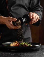 Crushed black peppercorns are being sprinkled over a dish from a glass grinder, adding spice. © Vitali