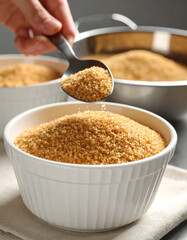 Golden brown sugar is being spooned into a mixing bowl, preparing for a sweet recipe.