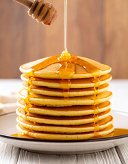A drizzle of honey falling slowly onto a stack of golden pancakes served on a plate.