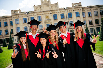 Photo of company groupmates students smile show v-sign mortarboard gown graduate college building...