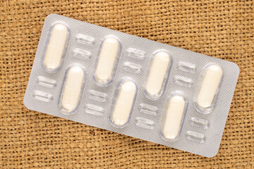Medical pills in blister packaging on jute cloth, close-up, top view.