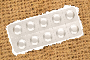 Medical pills in blister packaging on jute cloth, close-up, top view.