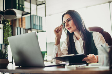 Fototapeta premium Experienced businesswoman working in an elegant office setting, wearing formal attire and analyzing data on her laptop