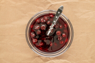 Cherry jam in a glass plate on a paper bag, top view, macro.